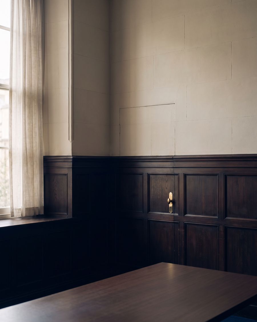 A quiet panelled room, unoccupied, with soft daylight falling through a tall window.