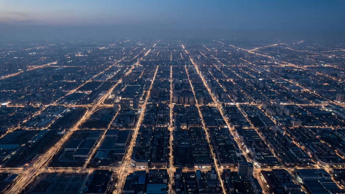 A dense city seen from high above at dusk, its lit avenues reading as a fine web of light.